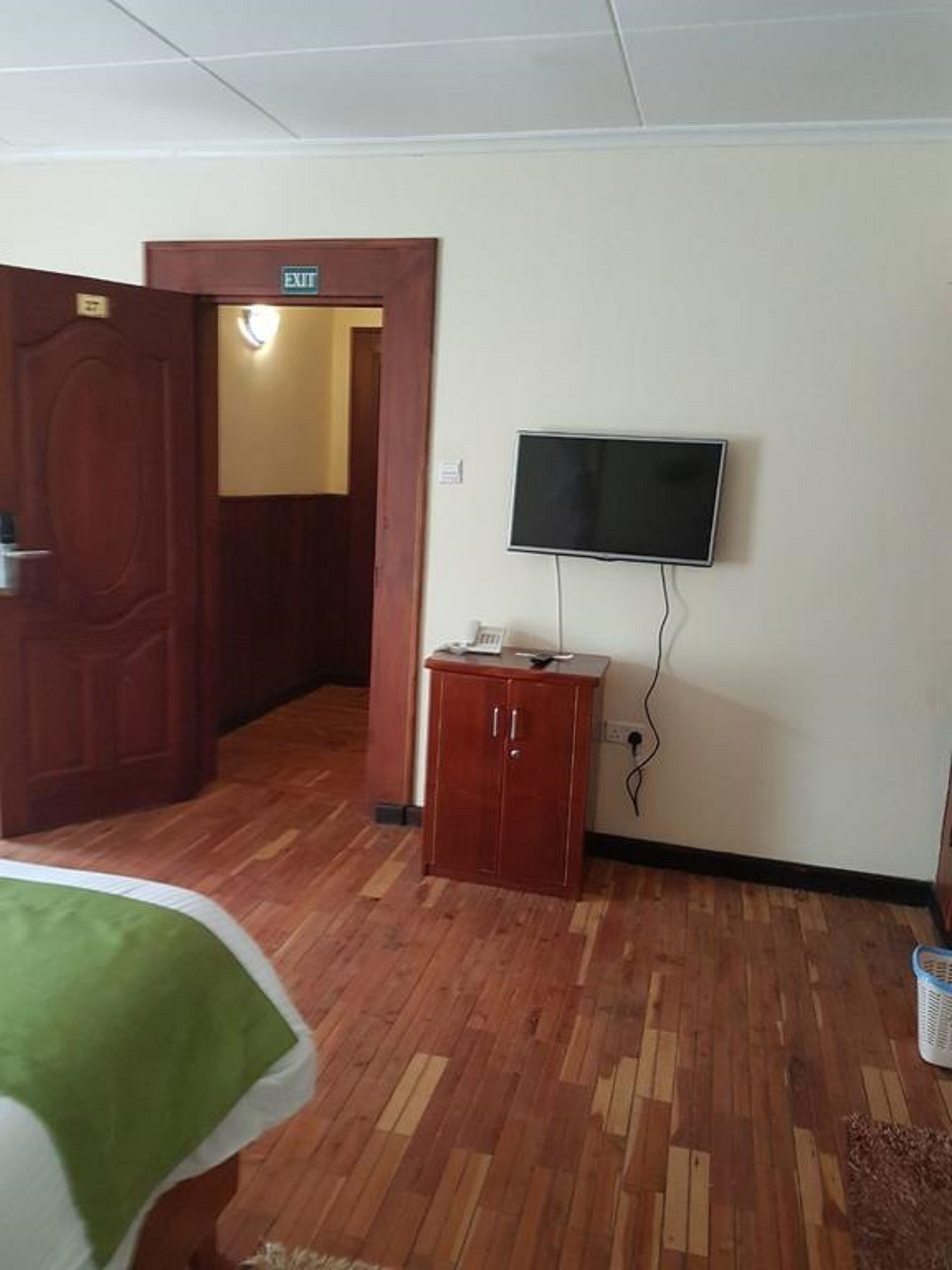 Ein Hotelzimmer mit Holzboden, einem an der Wand befestigten Fernseher, einer kleinen Kommode und einer Ausgangstür.