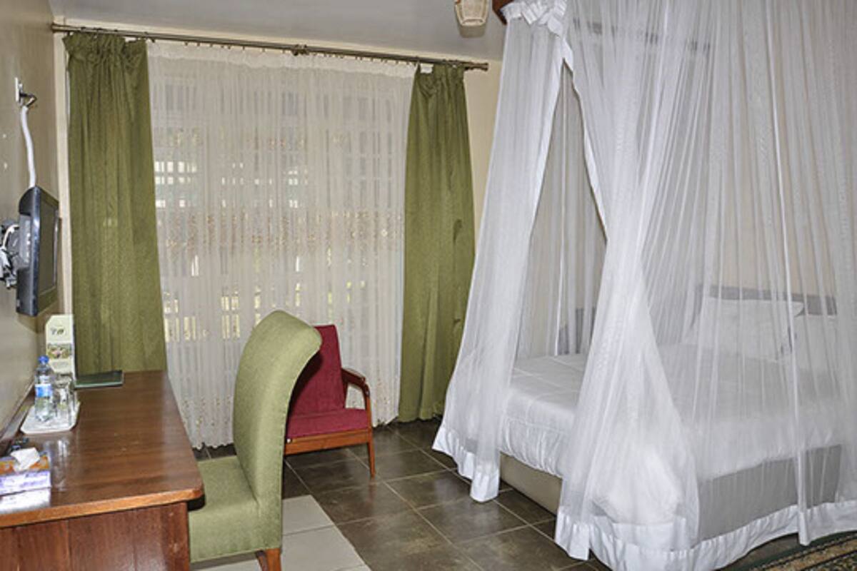 A room with a wooden desk, a green armchair, a bed with a white canopy, and a window with green curtains.