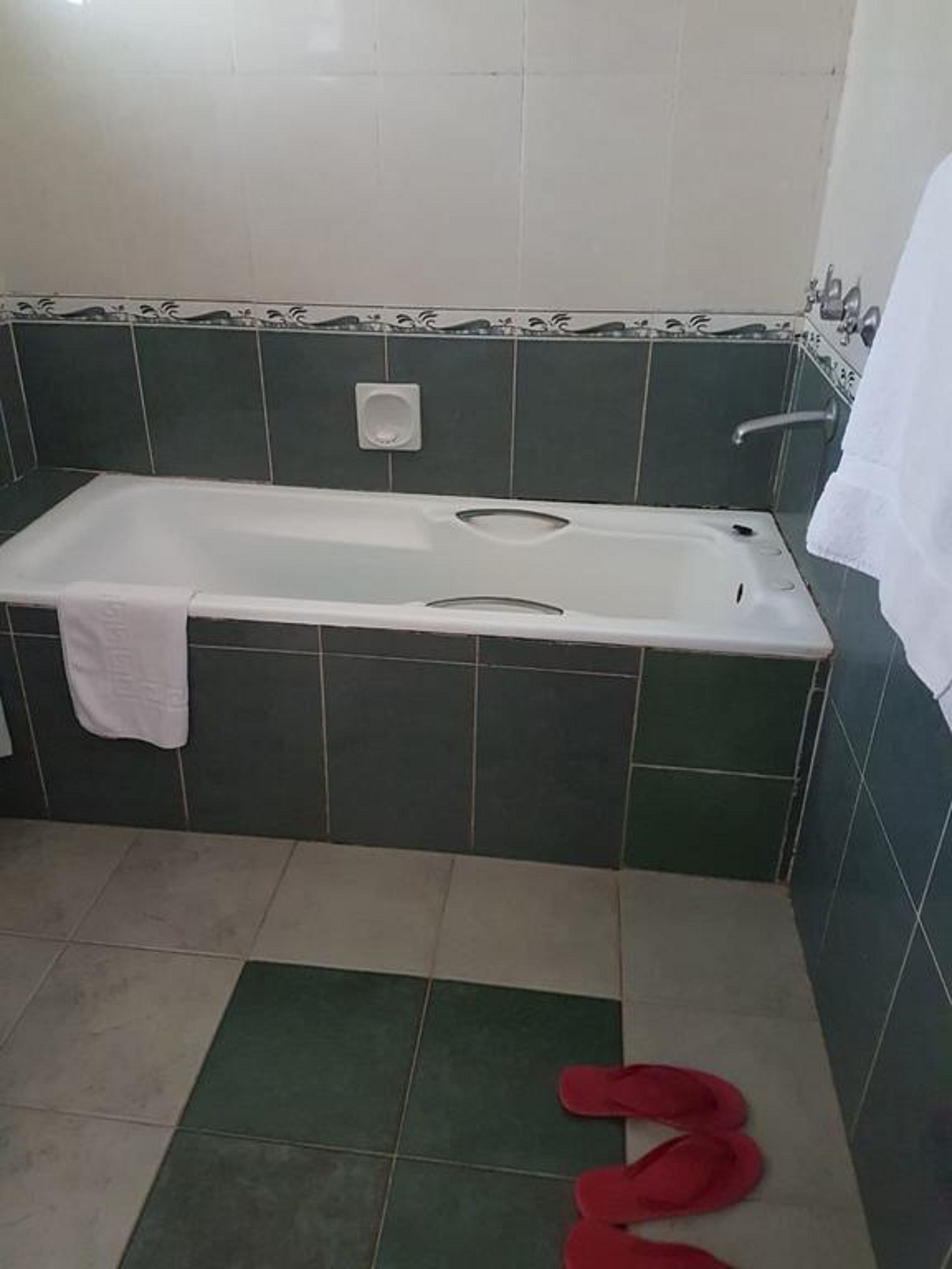 A bathroom with a bathtub, a white towel hanging on the wall, and a red object on the floor.