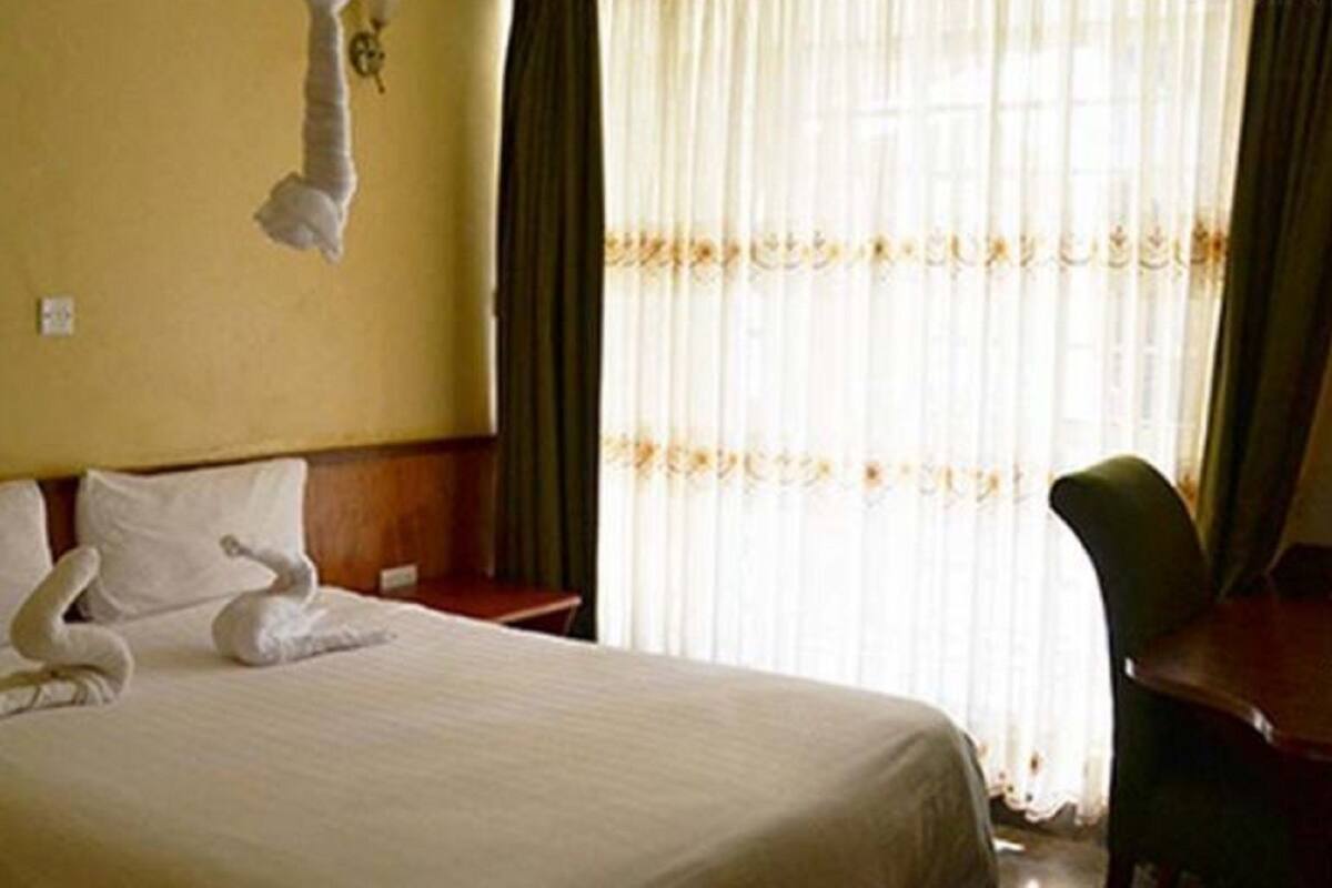 A hotel room with a bed, a chair, and a window with curtains.