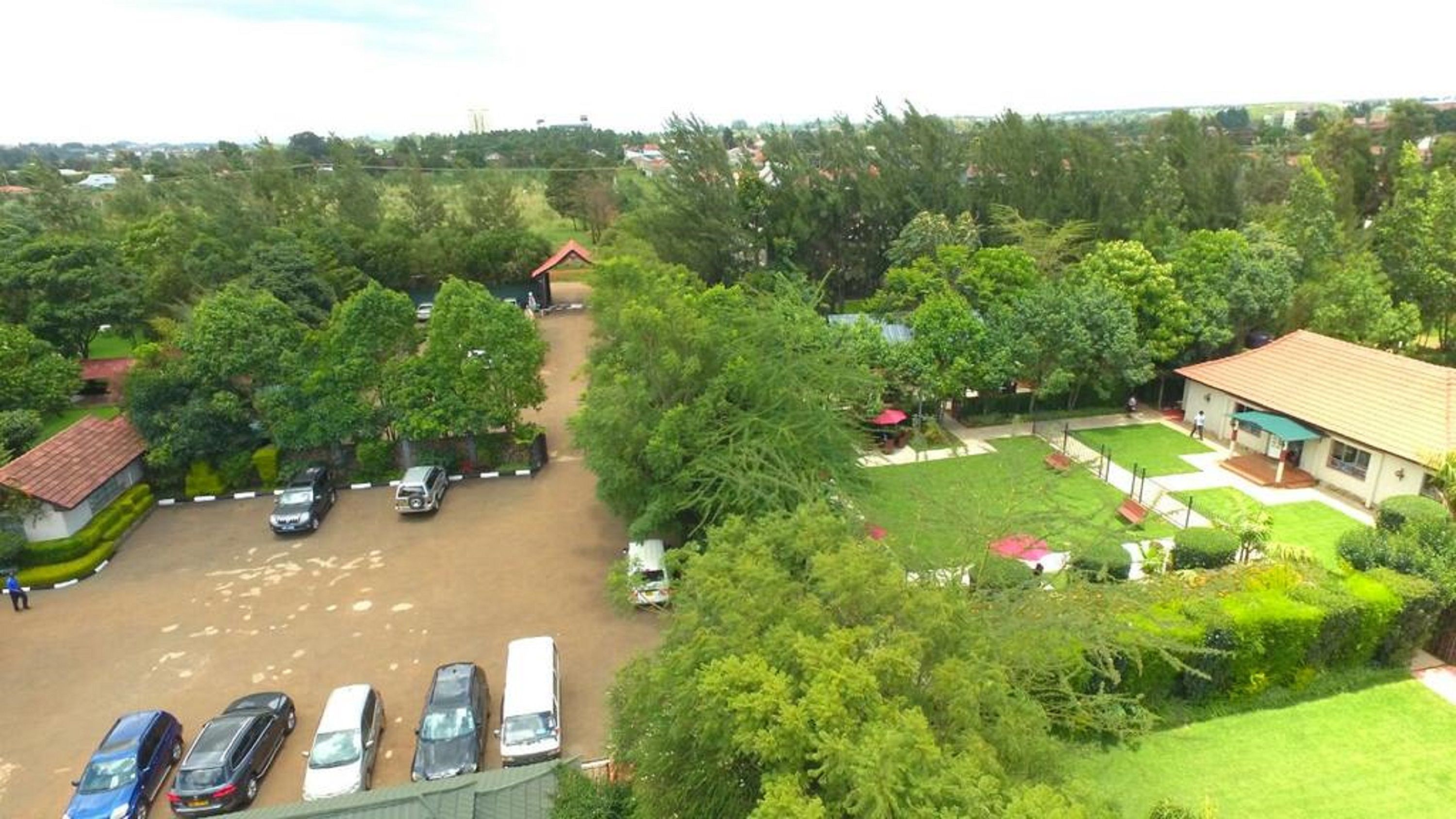 A parking area with several cars, surrounded by trees and a building with a red roof.