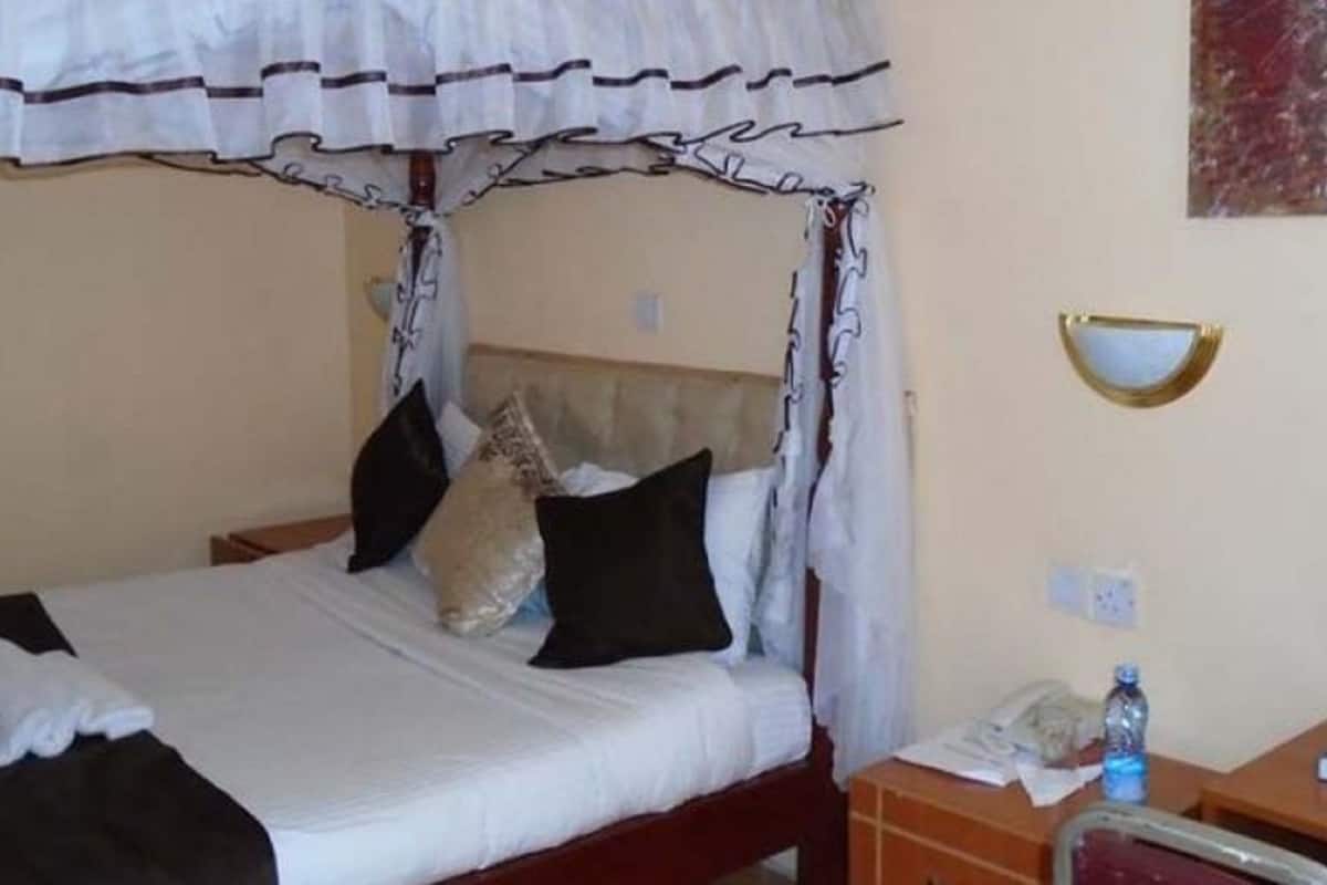 A hotel room with a bed, a bedside table with a phone, a mirror, and a wall-mounted light fixture.