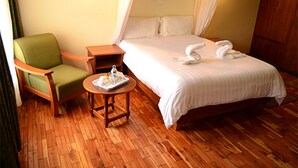 A hotel room with a bed, a green armchair, a wooden nightstand, and a small round table with a tray of items. - The Noble Hotel and Conference Center (Eldoret)