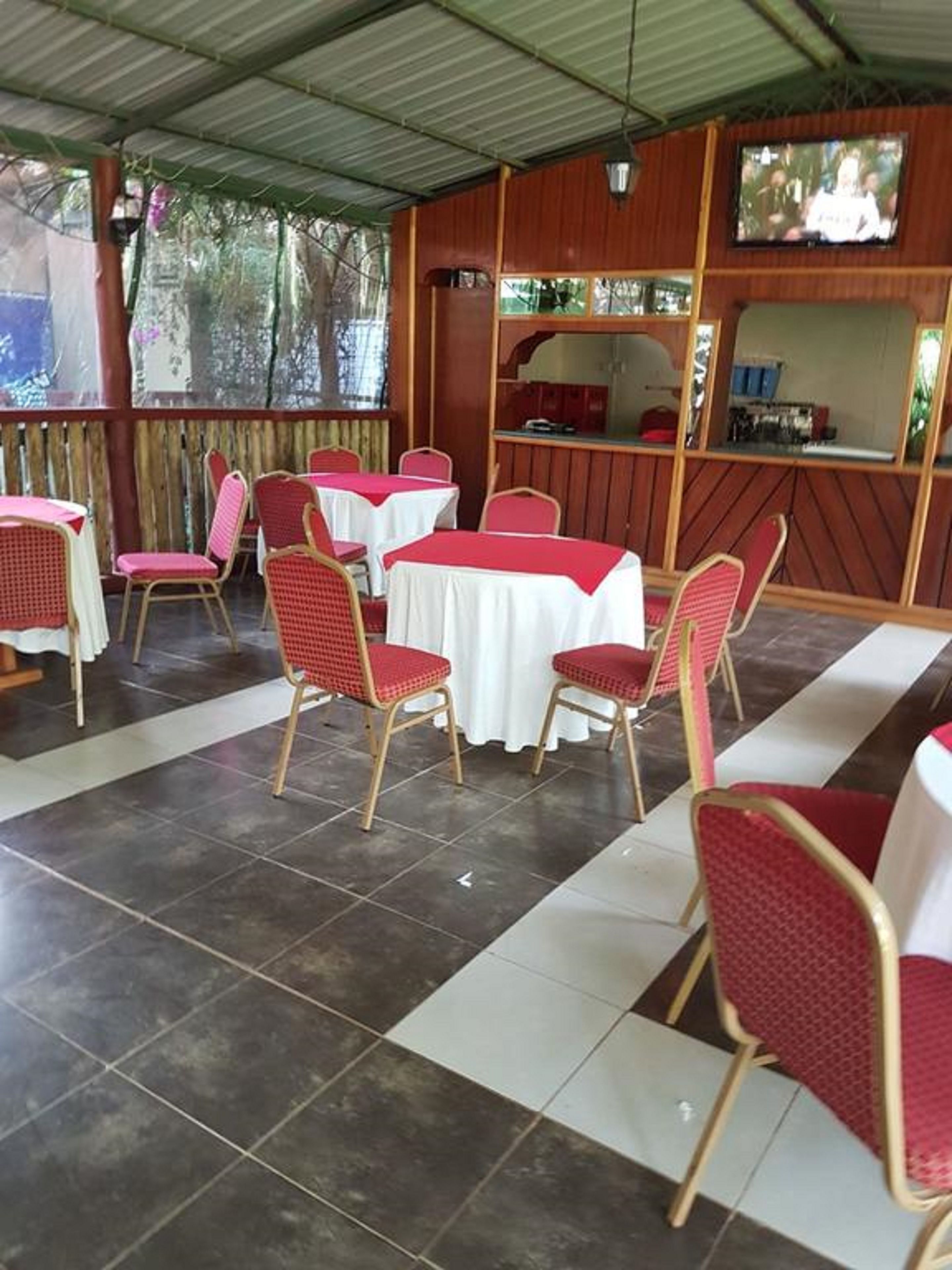Un'area pranzo all'aperto coperta, con tavoli e sedie, uno schermo televisivo e vista sugli alberi.