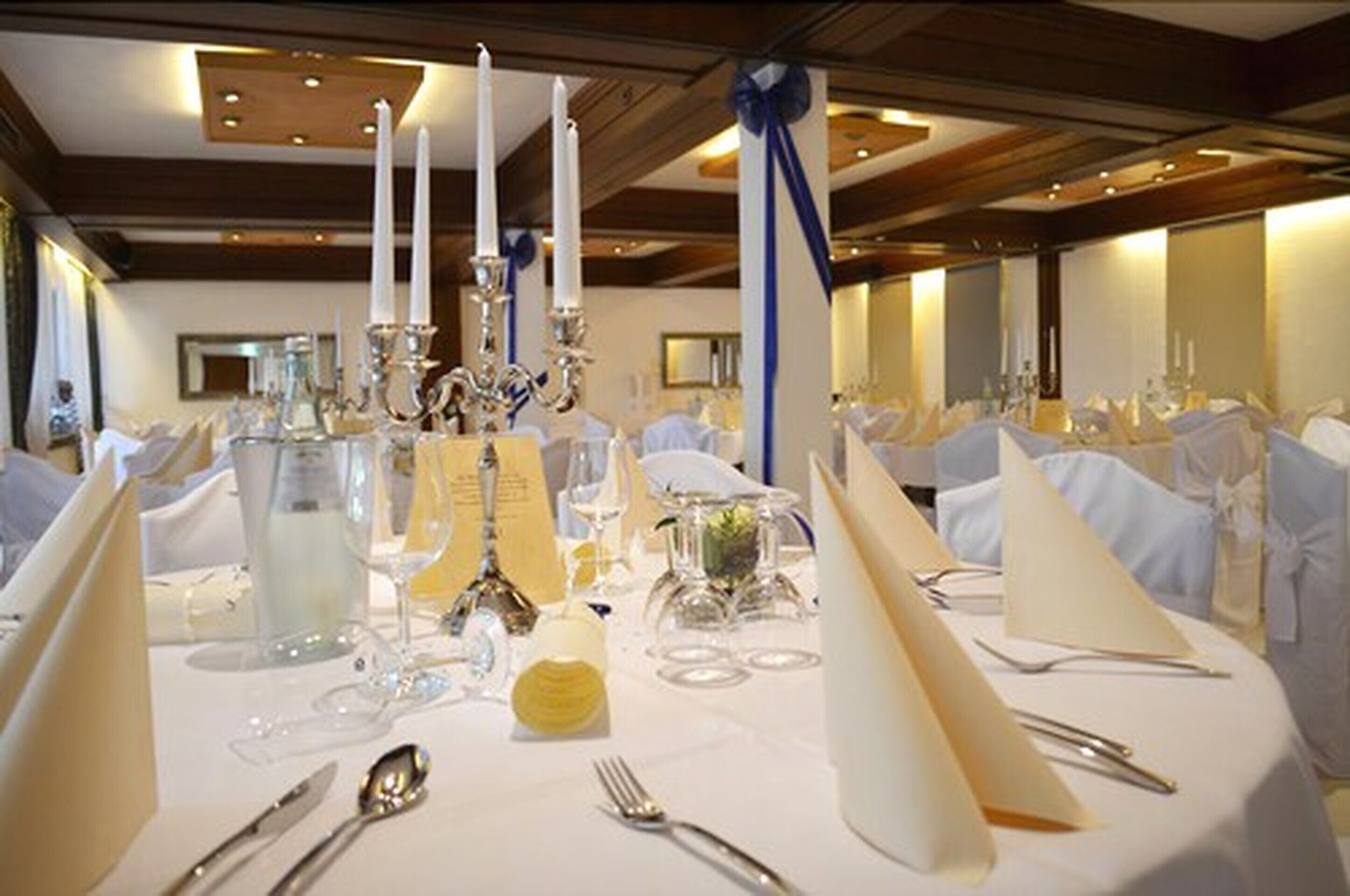 A banquet table set for a formal event with white tablecloths, silverware, and glassware.