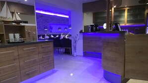 A modern kitchen with wooden cabinets, a central island, and a bar area with blue lighting. - Stadthotel Alsfeld (Alsfeld)