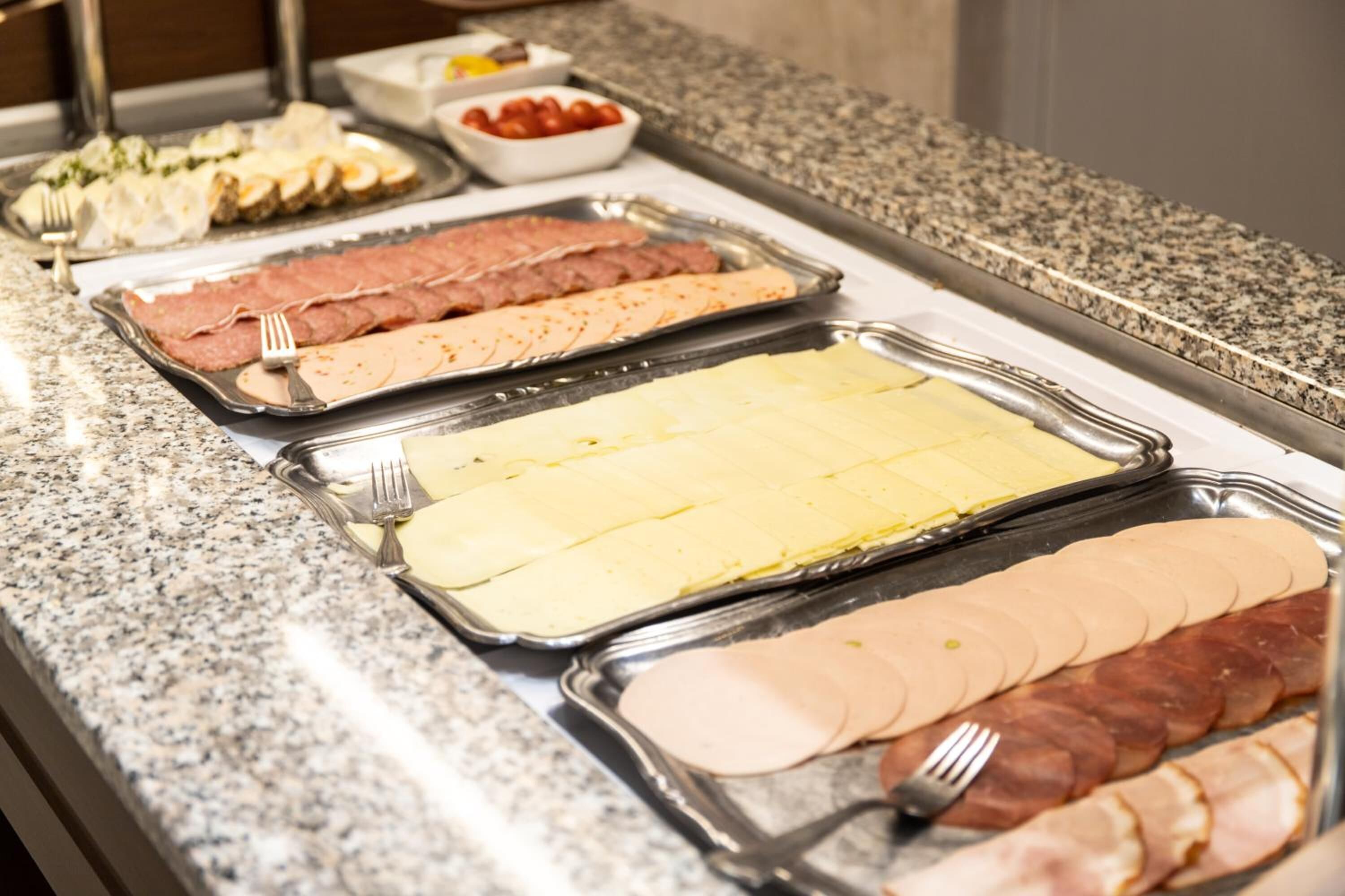 Un bufé con diversos tipos de carne y quesos en bandejas.