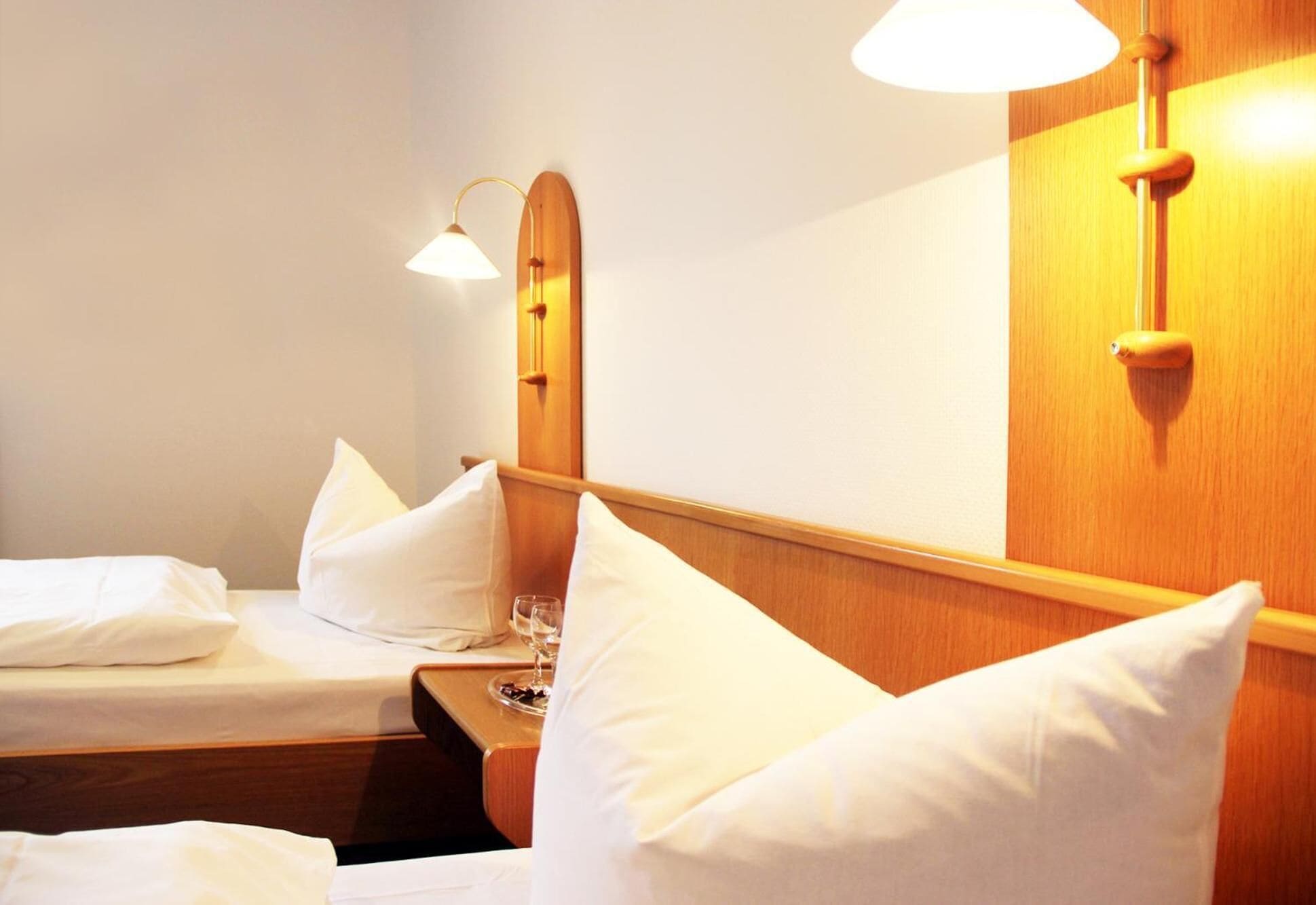 Ein Hotelzimmer mit zwei Betten, einem Holzkopfende und einem Spiegel mit Wandleuchten.