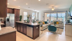 A modern kitchen with a central island, a dining area with a sofa and coffee table, and a living room with a large window.