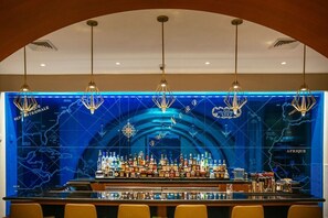 Eine Bar mit blauem Kartenhintergrund, mehreren hängenden Lampen und einer Auswahl an Flaschen.