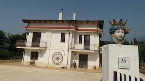A two-story building with a red-tiled roof, a balcony with a wrought iron railing, and a large decorative wheel on the ground floor. - L'Arcadia (Giffoni sei Casali)