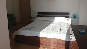 A neatly made bed with a white bedspread and a wooden headboard. There is a small table with a lamp and a picture frame on the wall. - L'Arcadia (Giffoni sei Casali)