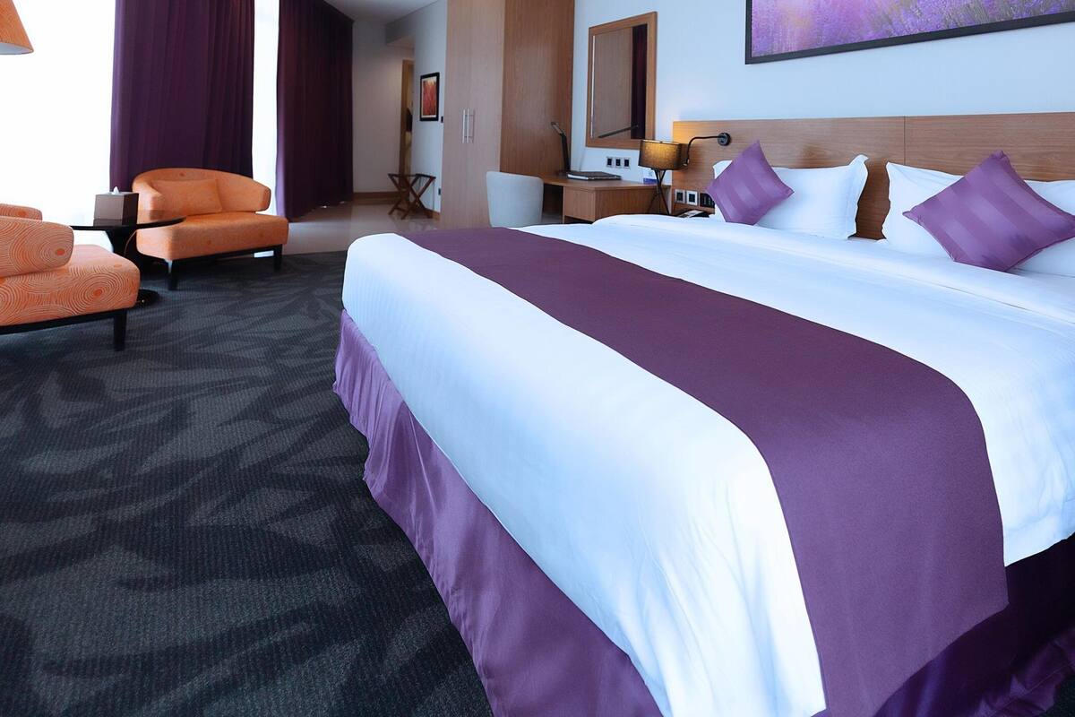 Ein Hotelzimmer mit einem großen Bett, einem Schreibtisch, einem Stuhl und Blick ins Freie.