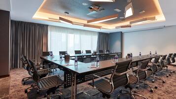 A conference room with a long table, multiple chairs, and a large window with curtains.