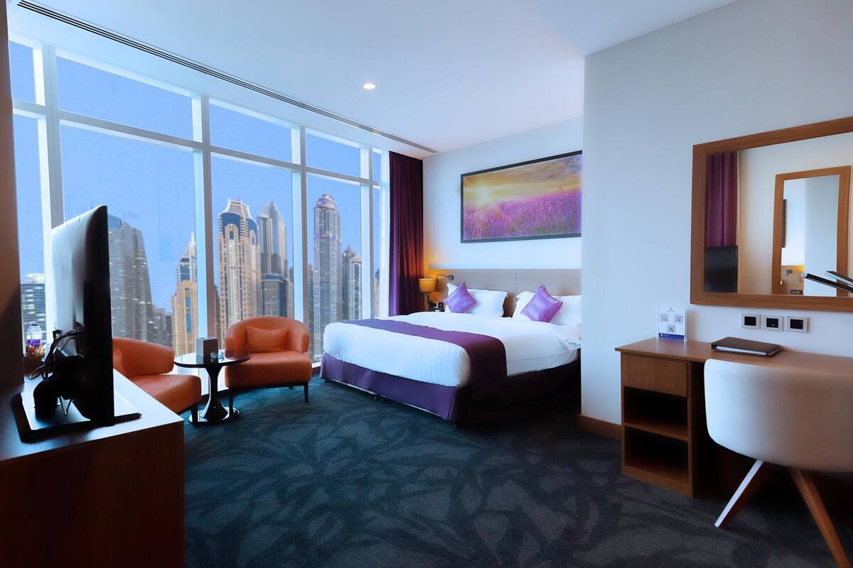 Ein Hotelzimmer mit großem Fenster, einem Bett, einem Schreibtisch und einem Sessel.