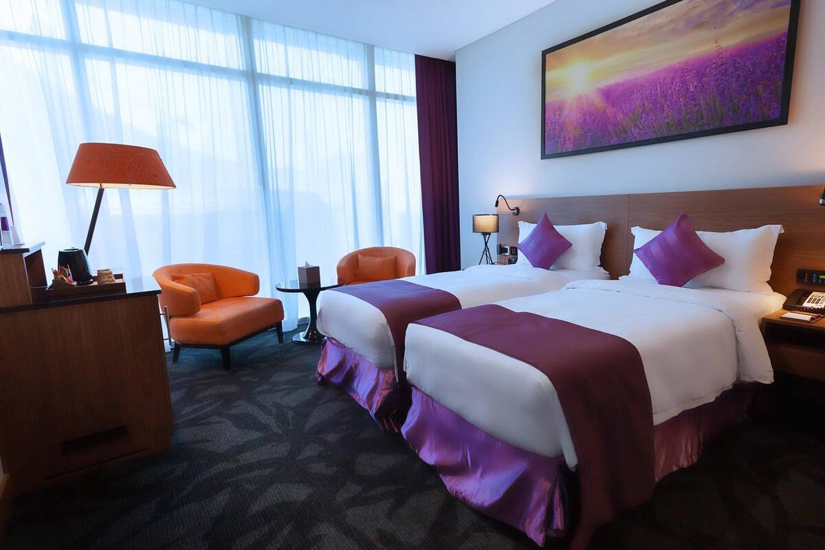 Ein Hotelzimmer mit zwei Betten, einem Schreibtisch, einem Stuhl und einem großen Fenster mit Vorhängen.