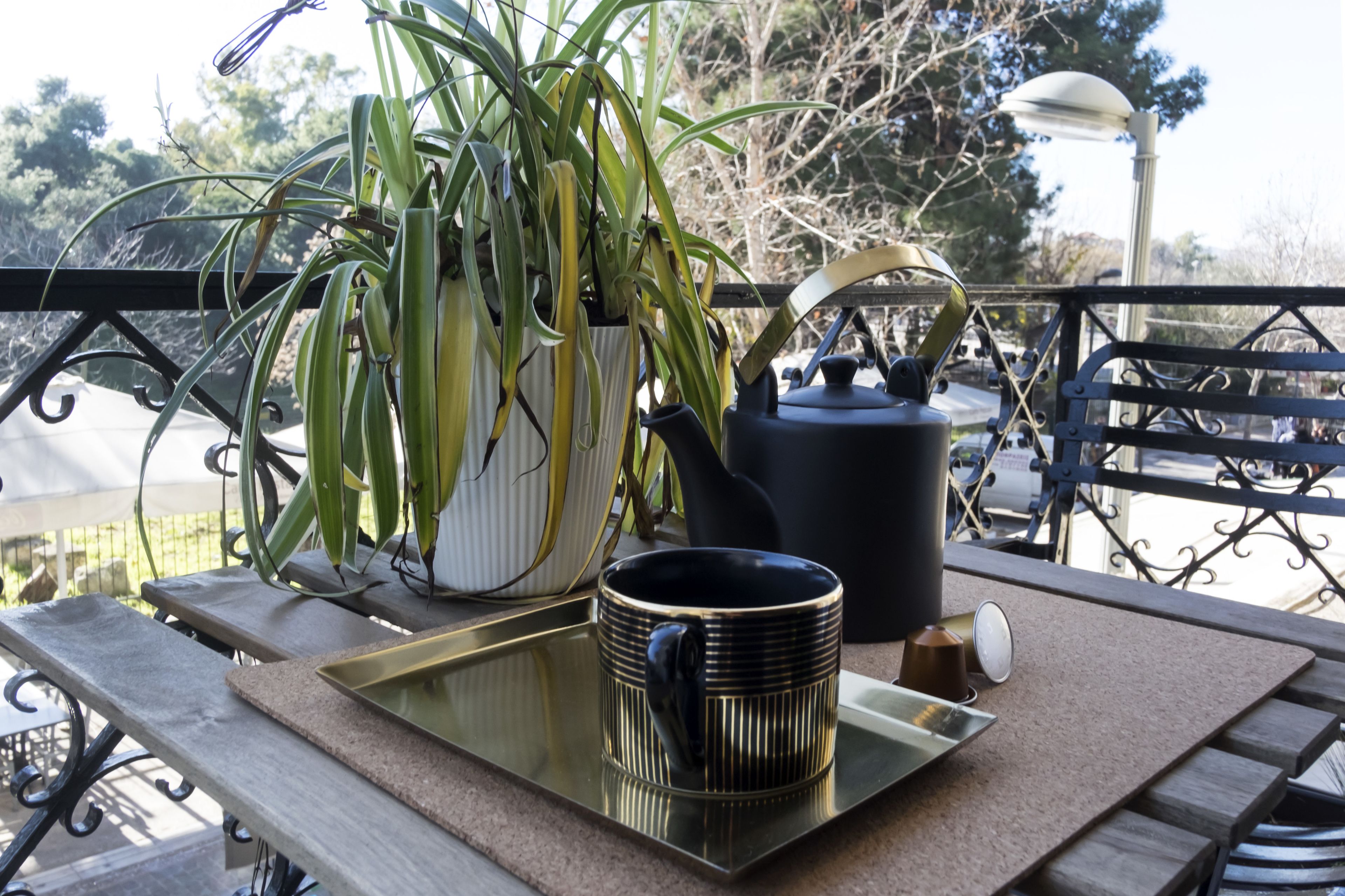A balcony with a table, a potted plant, a kettle, a mug, and a tray.