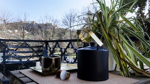 Um pátio com um banco de metal, uma mesa com uma cafeteira, uma caneca e um vaso de planta.