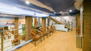 A spacious indoor area with wooden flooring, a staircase, and seating arrangements. - Caroline Hostel (Canggu)