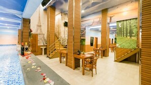 A restaurant with wooden paneling, tables, chairs, and a decorative ceiling mural. - Caroline Hostel (Canggu)