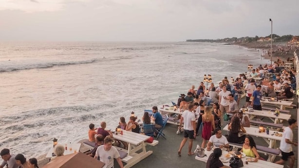 A crowded beachside restaurant with outdoor seating overlooking the ocean. - Caroline Hostel (Canggu)