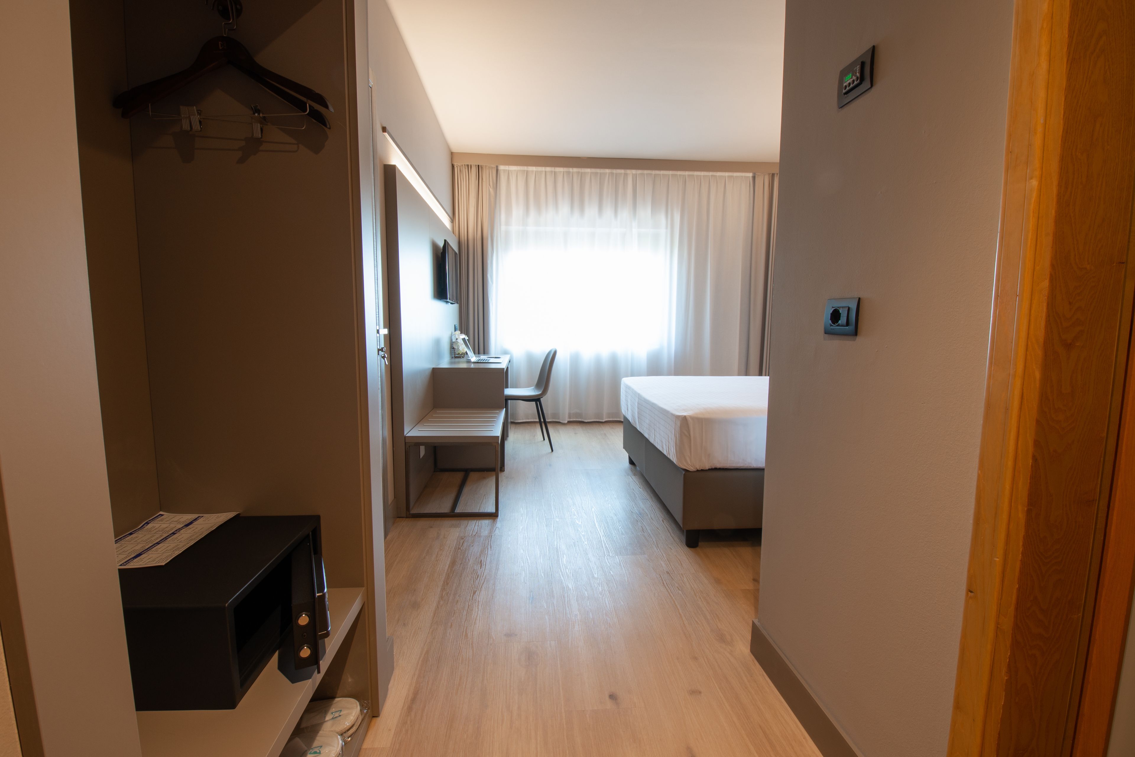 A hotel room with a bed, a desk, a chair, a TV, and a window with curtains.