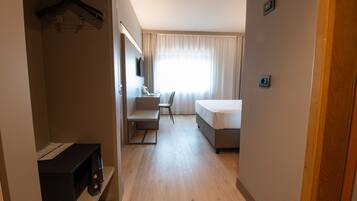 A hotel room with a bed, a desk, a chair, a TV, and a window with curtains.