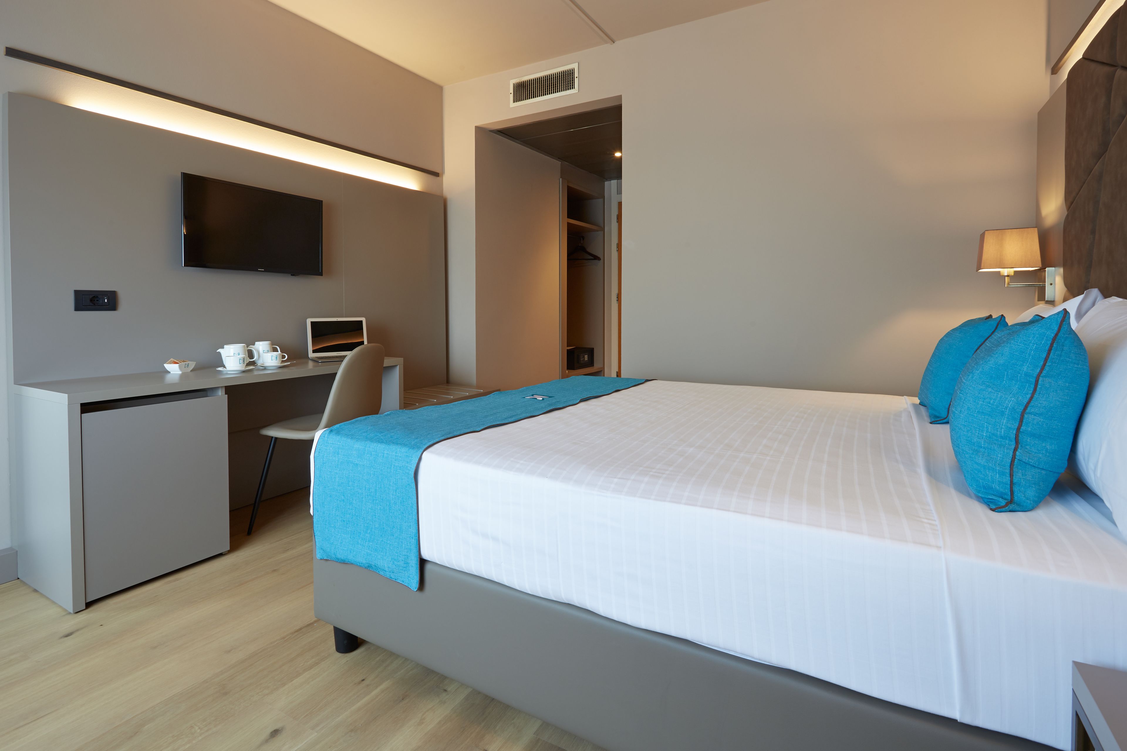 Una habitación de hotel moderna con cama, escritorio con computadora portátil, televisión y armario.