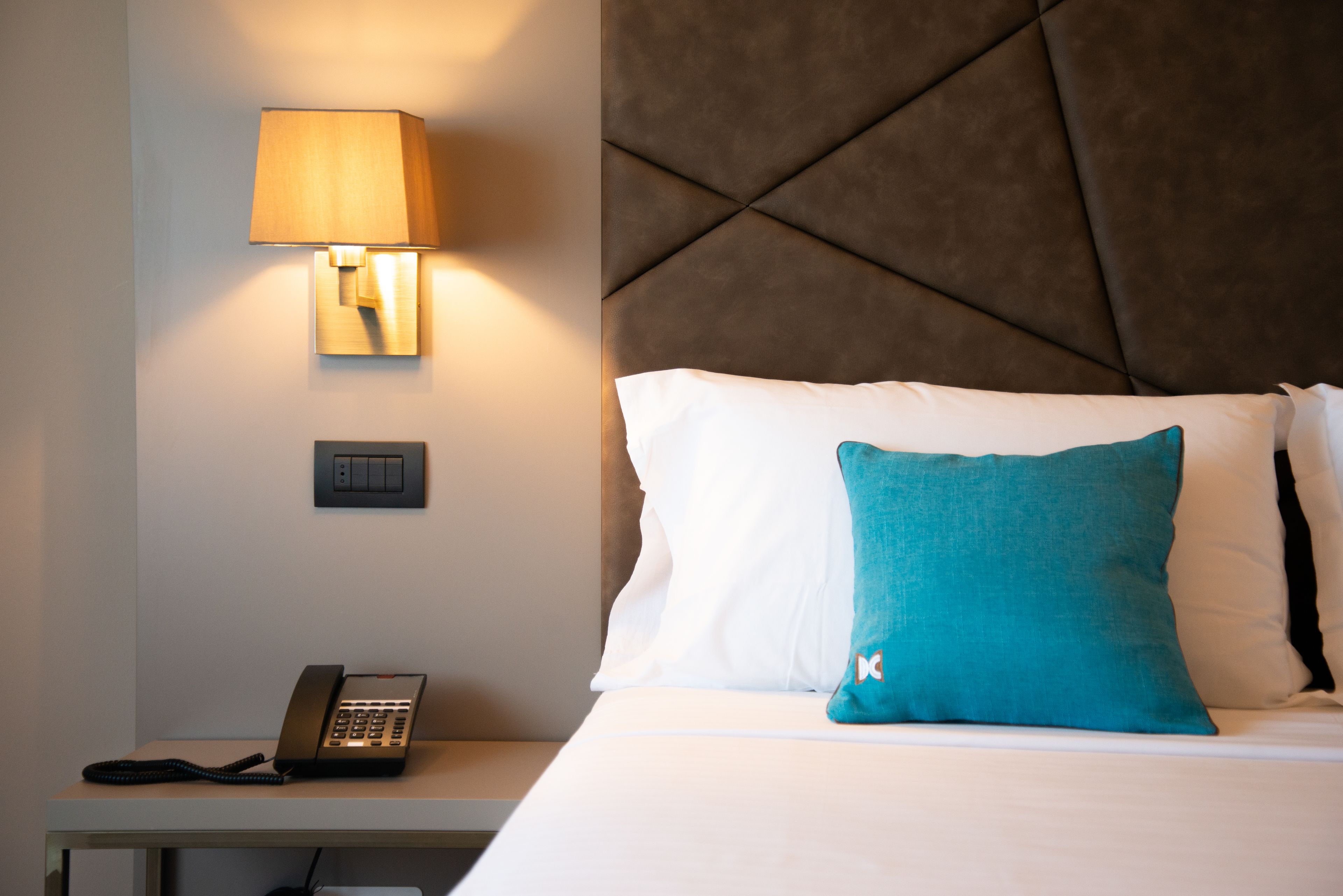 Una camera d'albergo con un letto, una lampada da comodino, un telefono e un interruttore della luce a parete.
