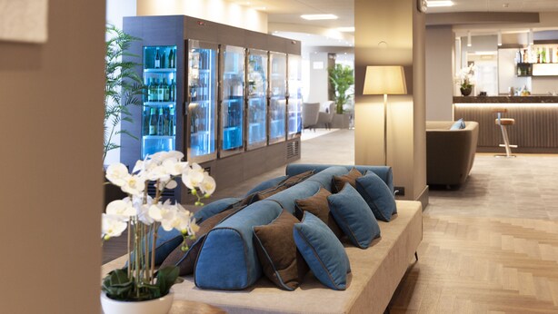 A modern lounge area with a sofa set, a small table with a potted orchid, and a bar area in the background. - DC Hotel International (Padova)