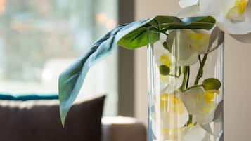 Eine klare Glasvase mit weißen Orchideen und einem einzelnen grünen Blatt, platziert auf einem Tisch neben einer weißen Tasse und Untertasse.