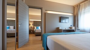 A hotel room with a large bed, a desk with a chair, a flat-screen TV, and a separate bedroom with a bed and nightstands. - DC Hotel International (Padova)