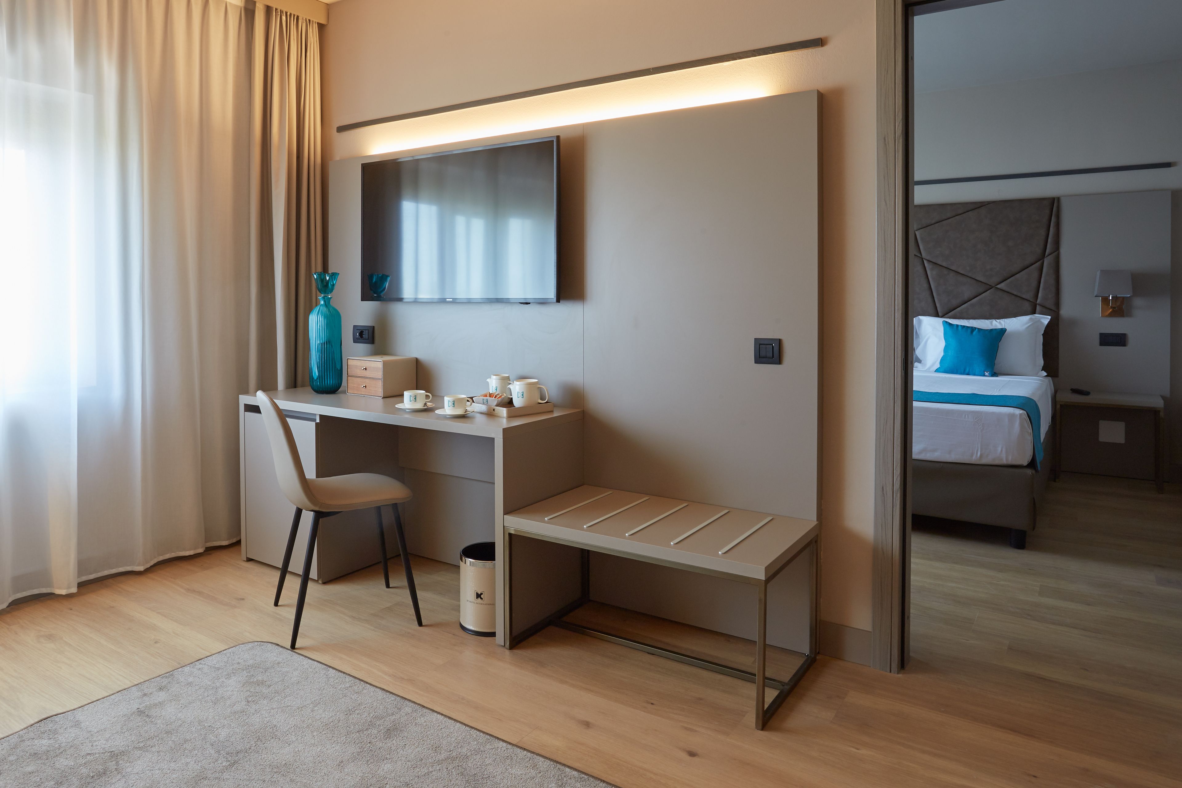 Een moderne hotelkamer met een bureau, stoel en een bed met een blauw kussen.