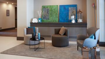 A modern lobby with a grey sofa, a round armchair, and a small table with candles. There are abstract paintings on the wall and a fire alarm sign.