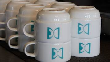 A row of white ceramic mugs with teal logos on a dark countertop.