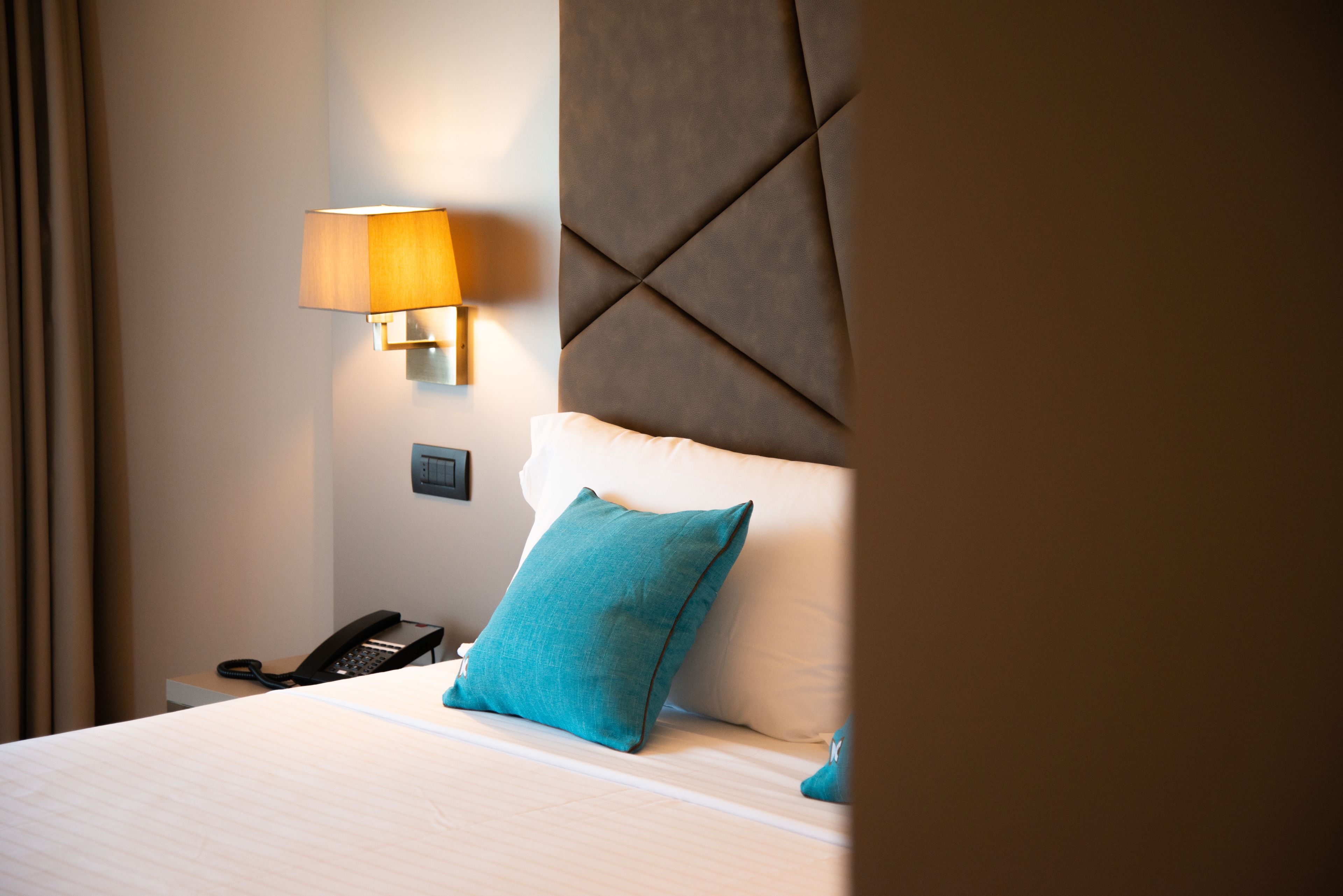A hotel room with a bed, a bedside lamp, a telephone, and a wall-mounted light fixture.