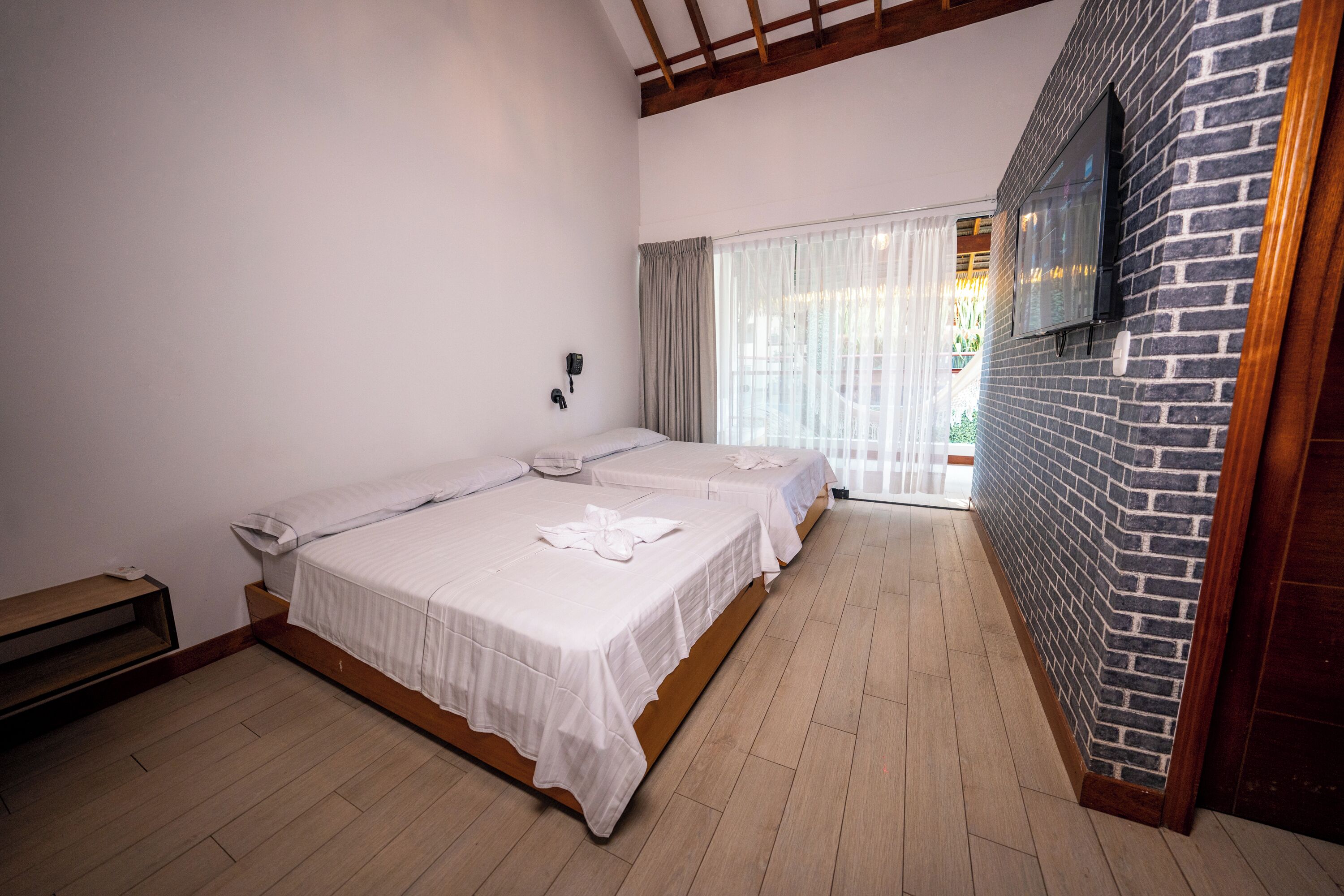 Une chambre d’hôtel avec deux lits, un plancher en bois, un mur en briques et un téléviseur fixé au mur.
