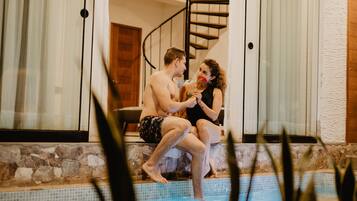 Una pareja sentada junto a una piscina con un muro de piedra y una escalera de caracol al fondo.