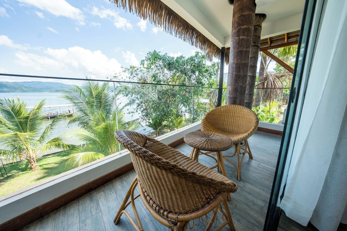 Een balkon met rieten meubilair, uitzicht op een meer en begroeiing.