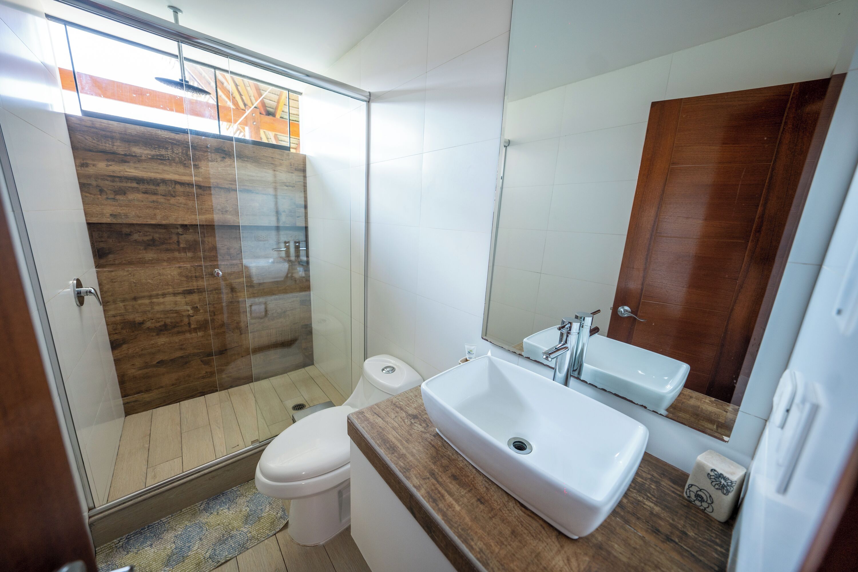 A modern bathroom with a glass shower enclosure, a wooden vanity, and a large mirror.