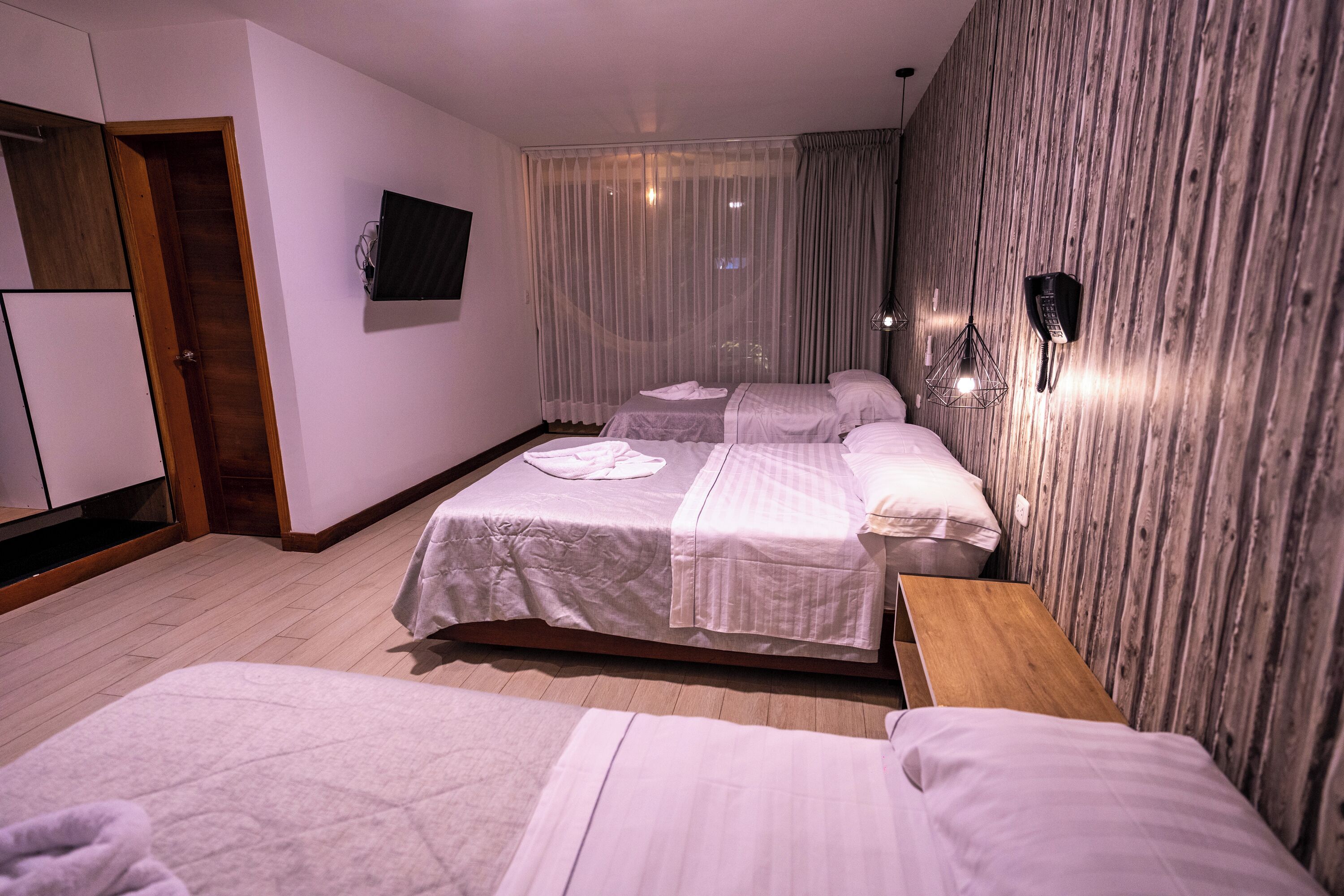 Habitación de hotel con dos camas, una pared de madera, televisor y ventana con cortinas.