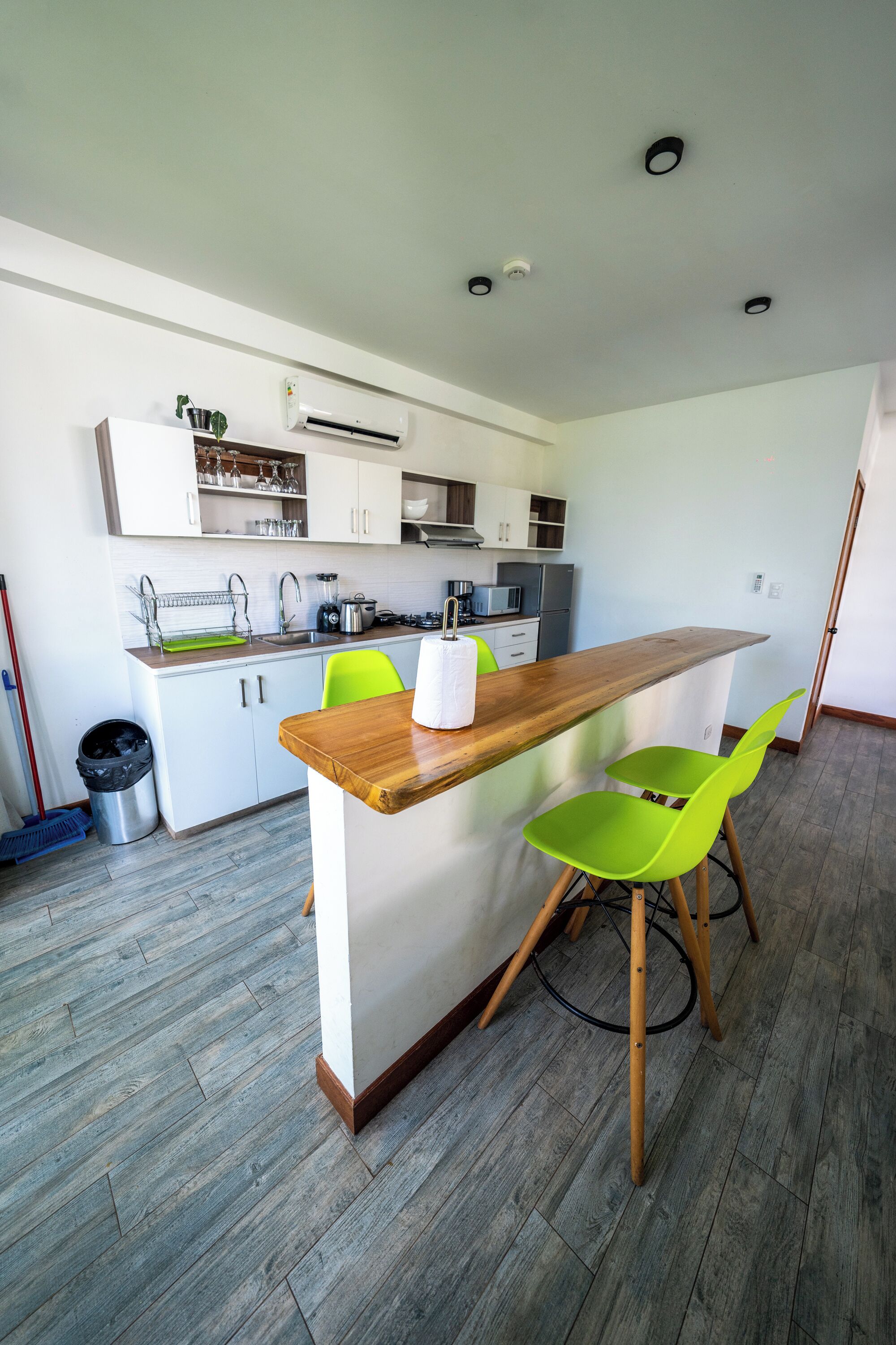 Una cocina moderna con armarios blancos, encimera de madera y una silla verde brillante.