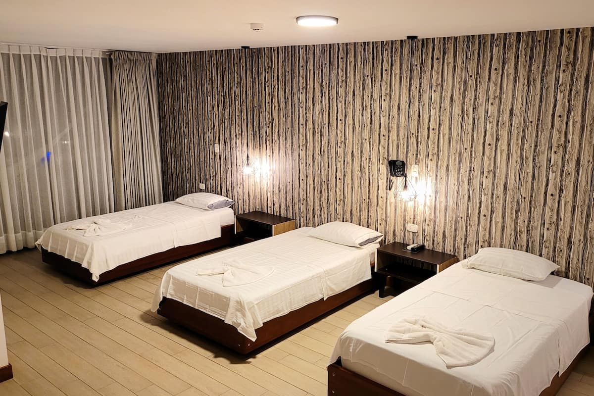 Een hotelkamer met drie eenpersoonsbedden, houten vloeren, een gordijn en een wand met verticale houten lambrisering.