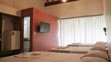 Habitación de hotel con dos camas, una pared de acento de ladrillo, un armario y una ventana con cortinas.