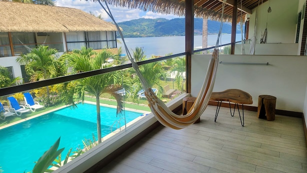 Een balkon met een hangmat, een zwembad en uitzicht op water en bergen.