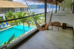 Un balcon avec un hamac, une piscine et une vue sur l’eau et les montagnes.