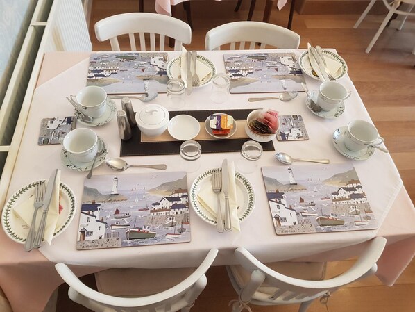 A dining table set with plates, cutlery, and glasses, surrounded by white chairs. - Rosemead Guest house (Paignton)