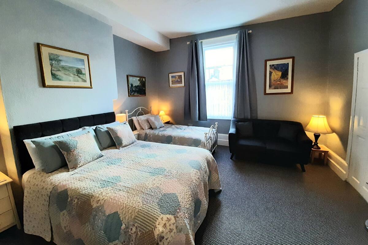 A hotel room with two beds, a sofa, and a window with curtains.