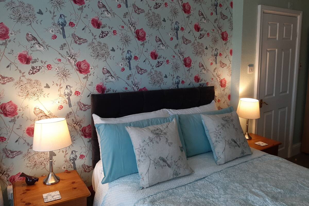 A bedroom with floral wallpaper, a dark headboard, and two bedside lamps.