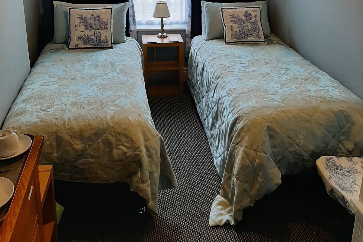 A room with two beds, a small table, a lamp, and a window with curtains.